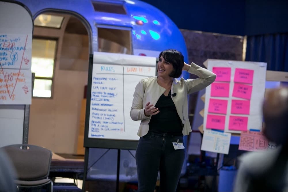 Sura at a flip chart beside an Airstream trailer during a workshop