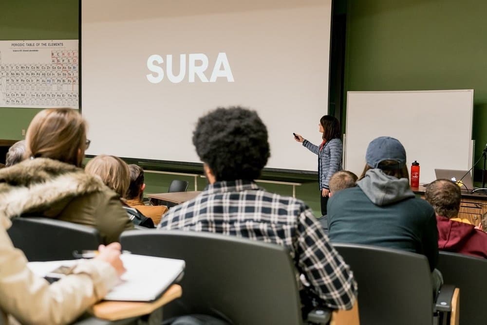Sura lecturing in a hall with her name on the screen